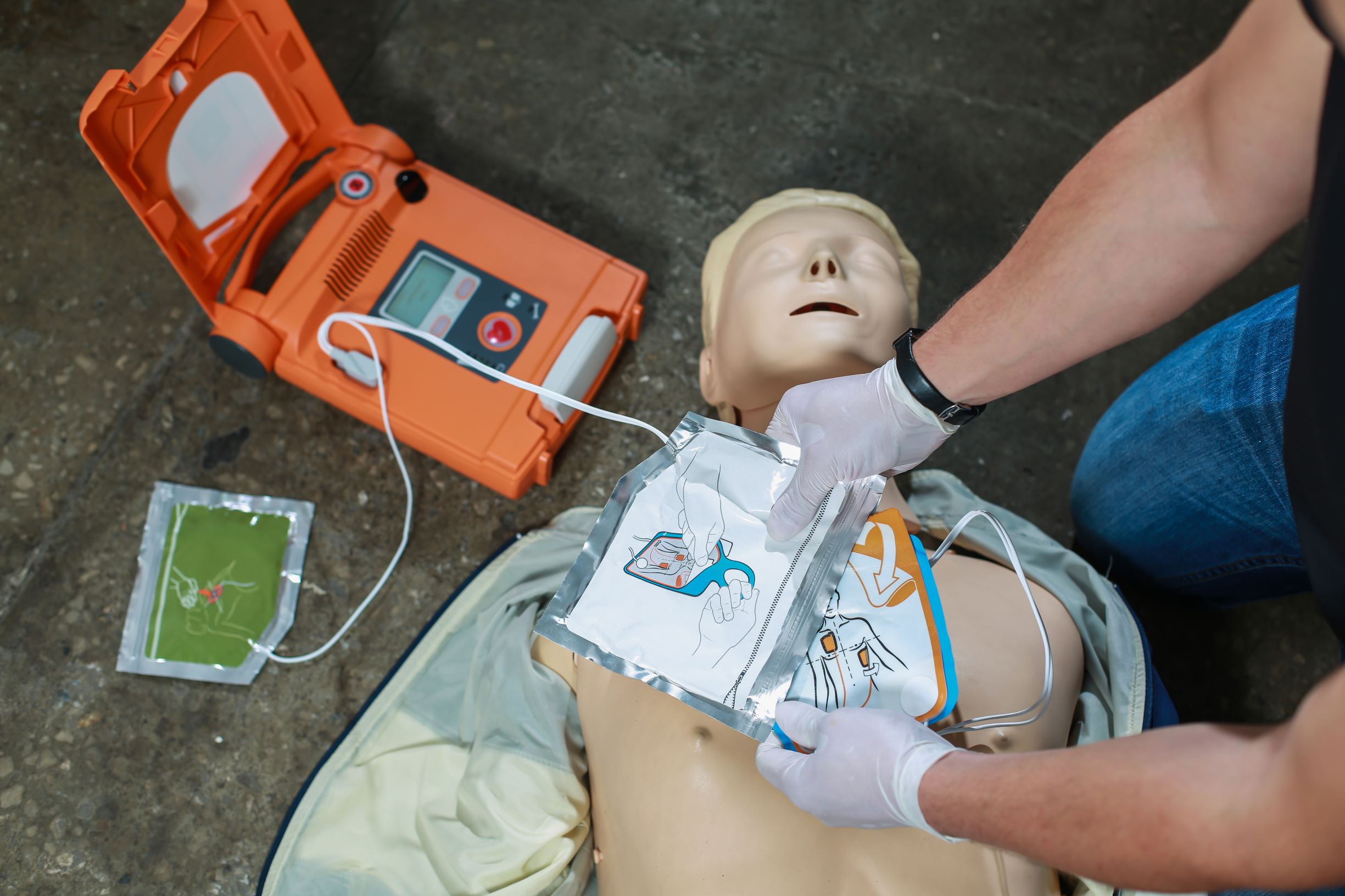 gloved hands practicing applying AED electrode pads onto a CPR manikin